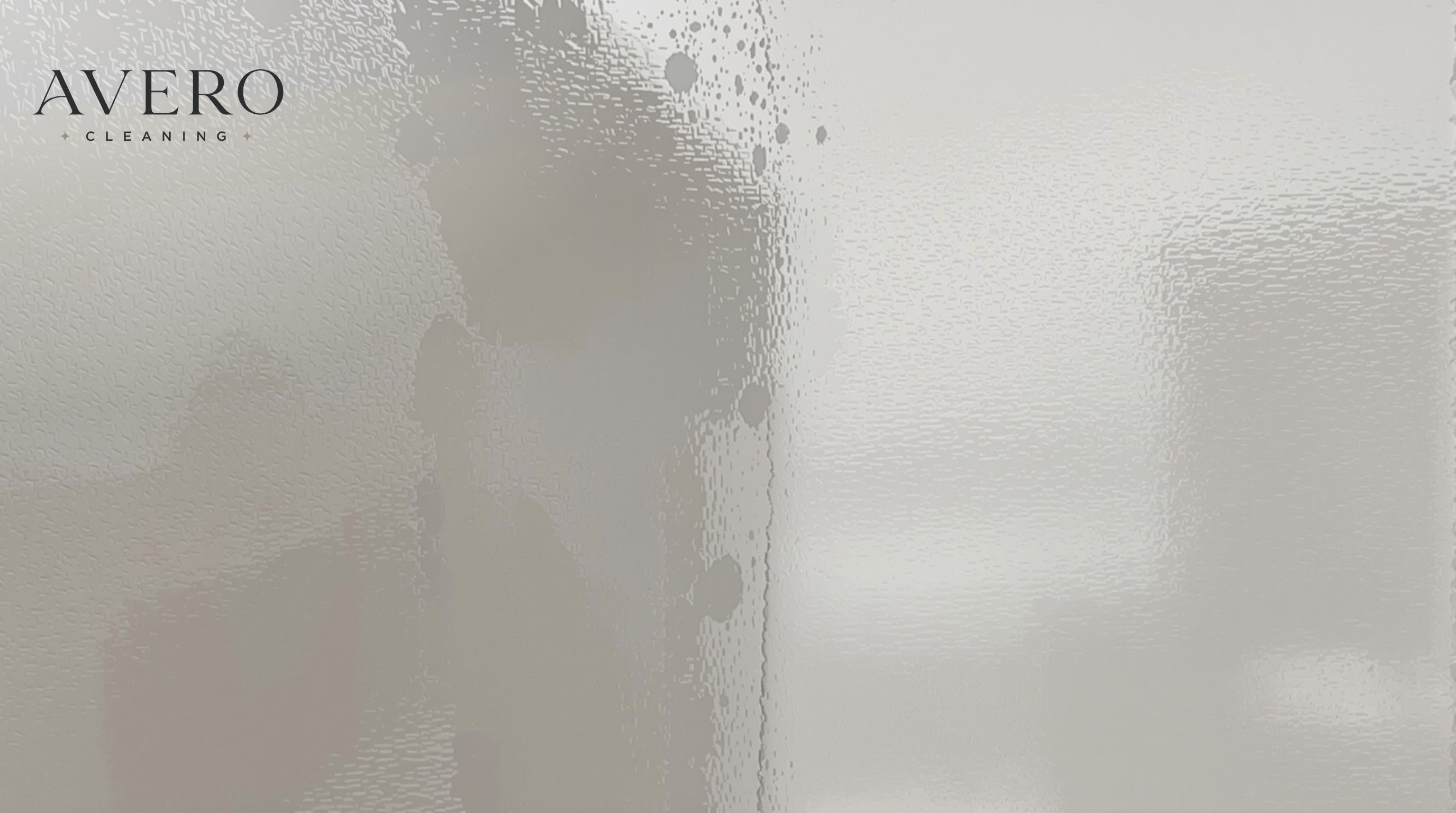 A shower glass door being cleaned, one side clear and one side still cloudy with soap scum